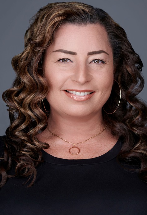 Photo of Cynthia Miller (a woman with brown curly hair wearing a gold necklace and a black dress)